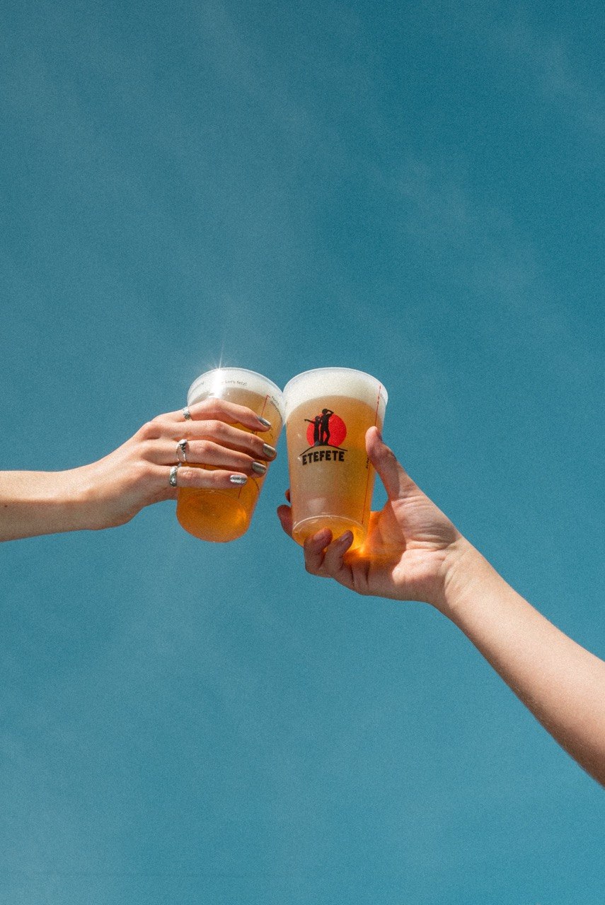 ETEFETE Sommermotiv mit anstoßenden Bierbechern vor blauem Himmel